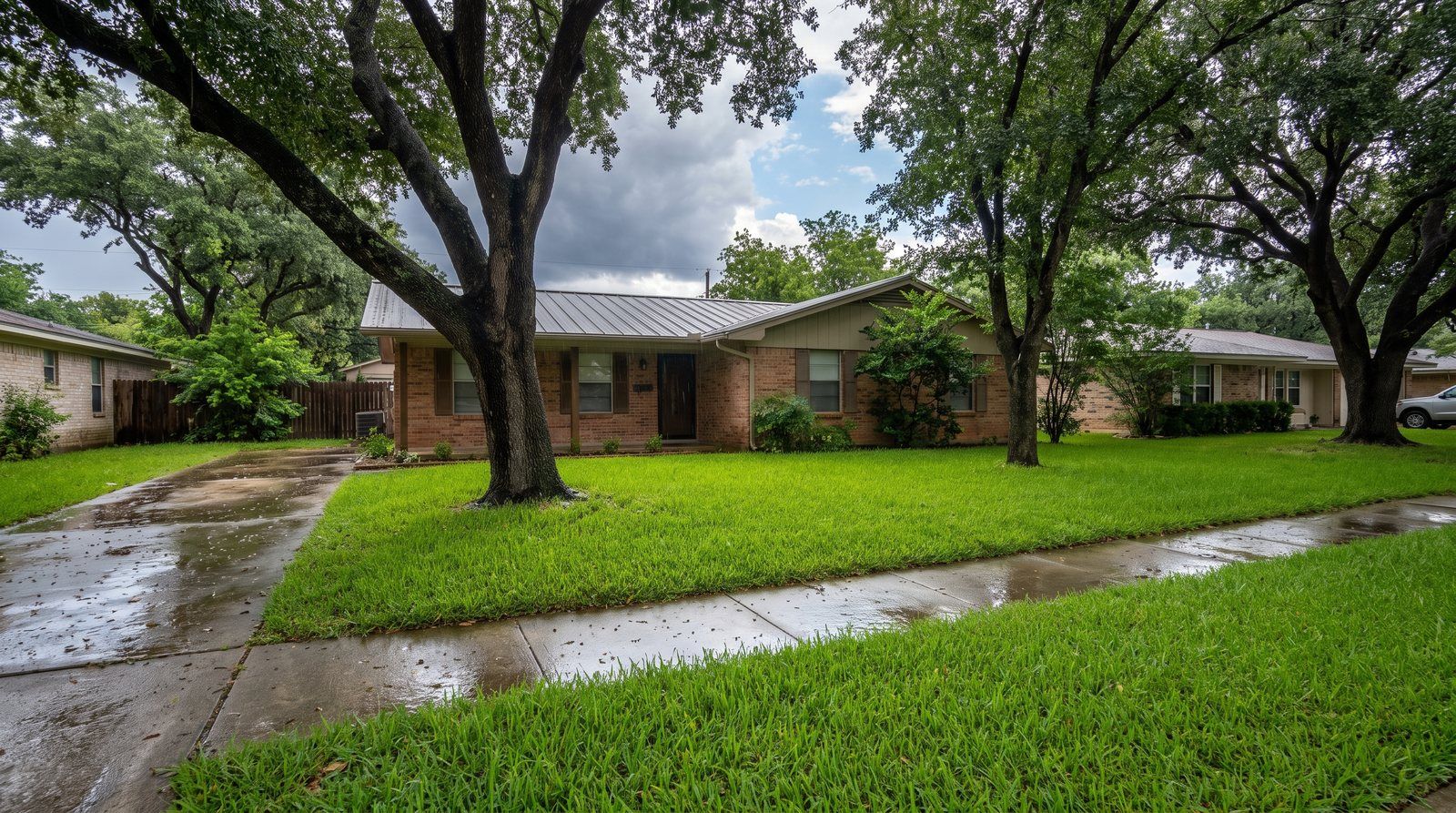 A lush St. Augustine front lawn glistening with raindrops just after a storm, wet sidewalk and a clearing sky over a brick ranch house