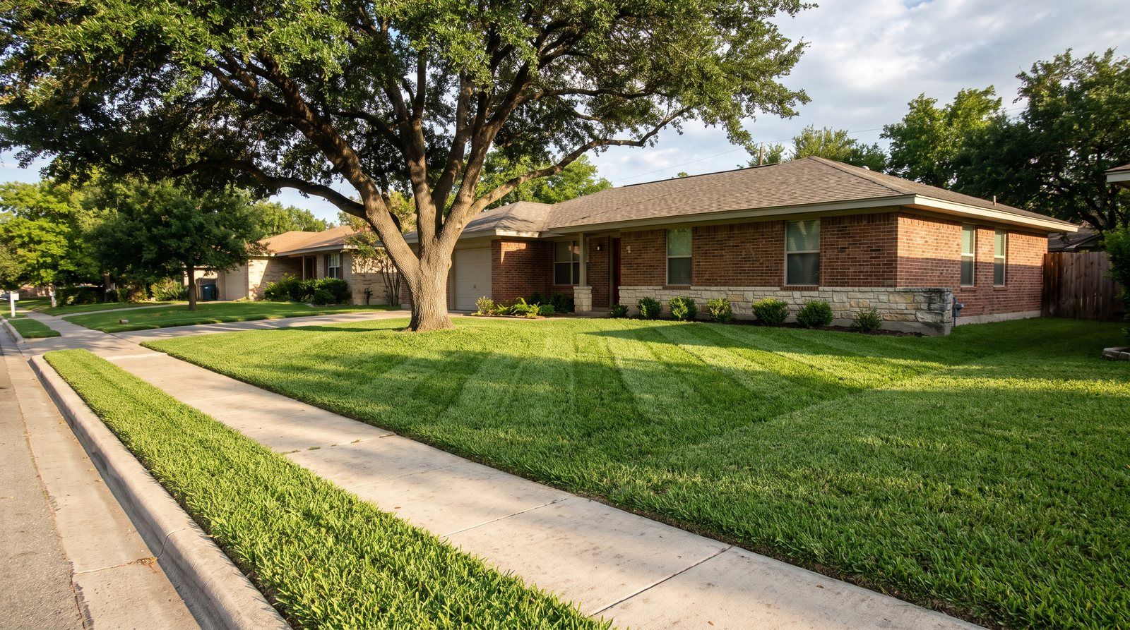 A freshly mowed St. Augustine front lawn with neat mowing stripes and a crisp edged sidewalk in front of a brick ranch house